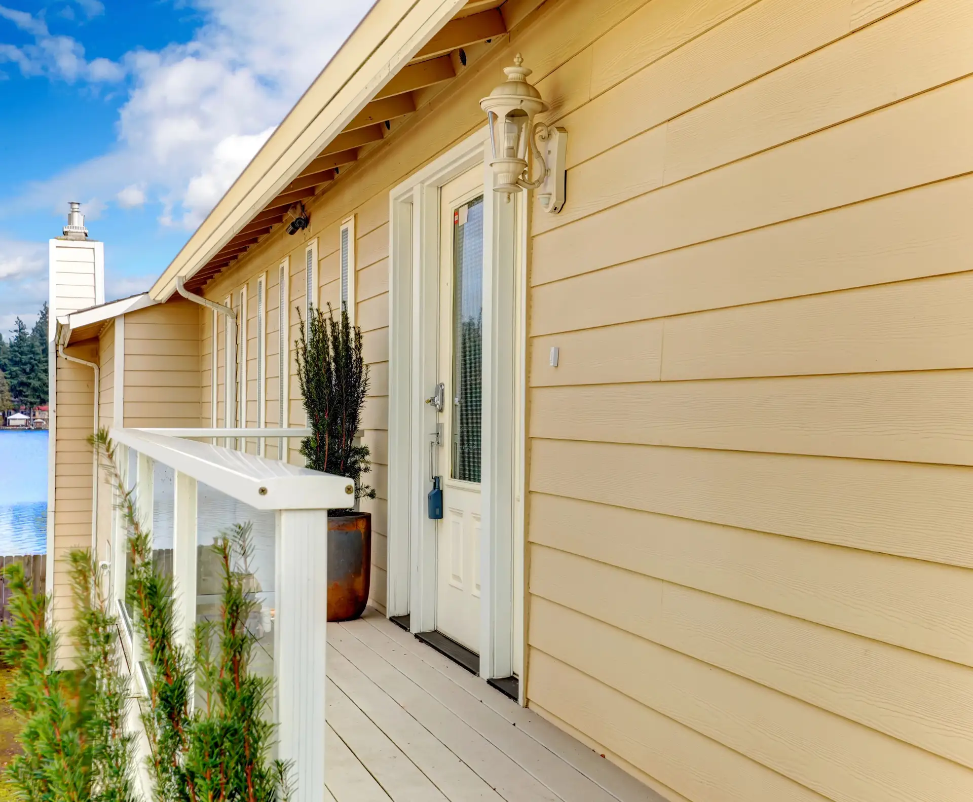 Pale yellow lap siding beside a front door and a deck with glass railing