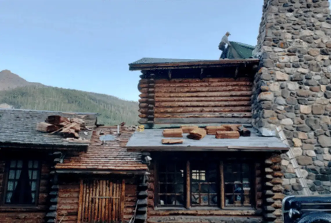 Roofer on a historic log building with new wood shakes stacked on the roof