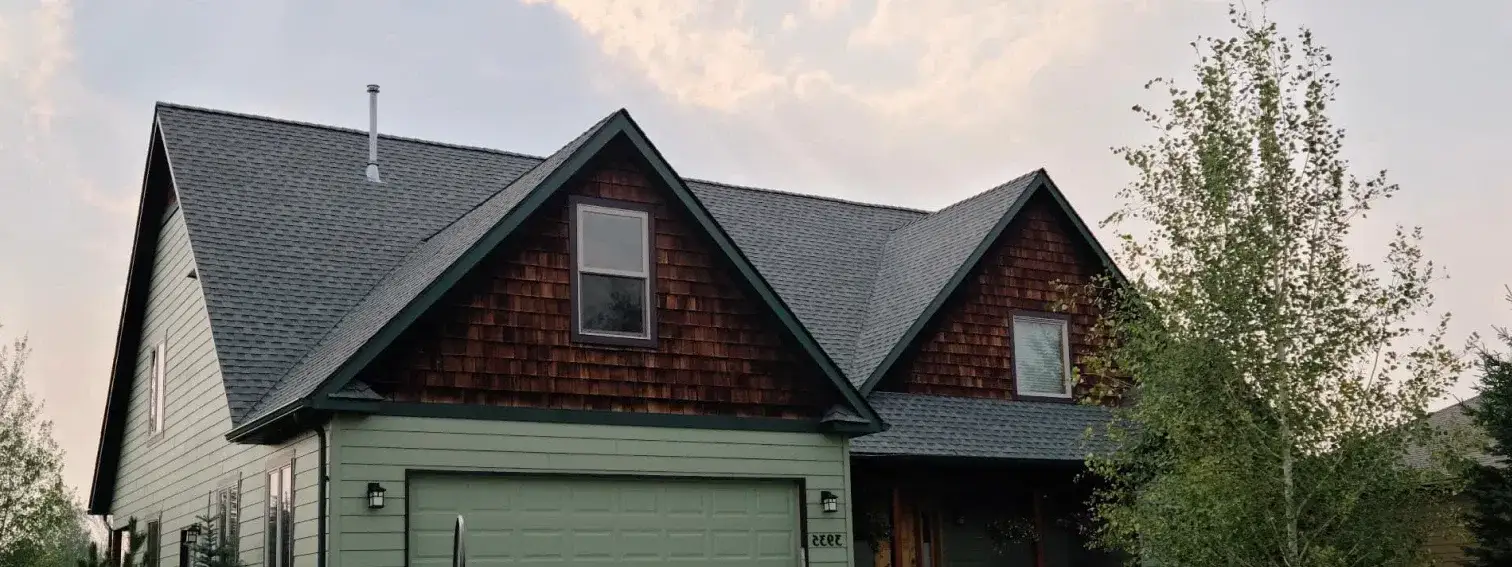 Two-storey green home with a dark shingle roof and cedar shake gables at dusk