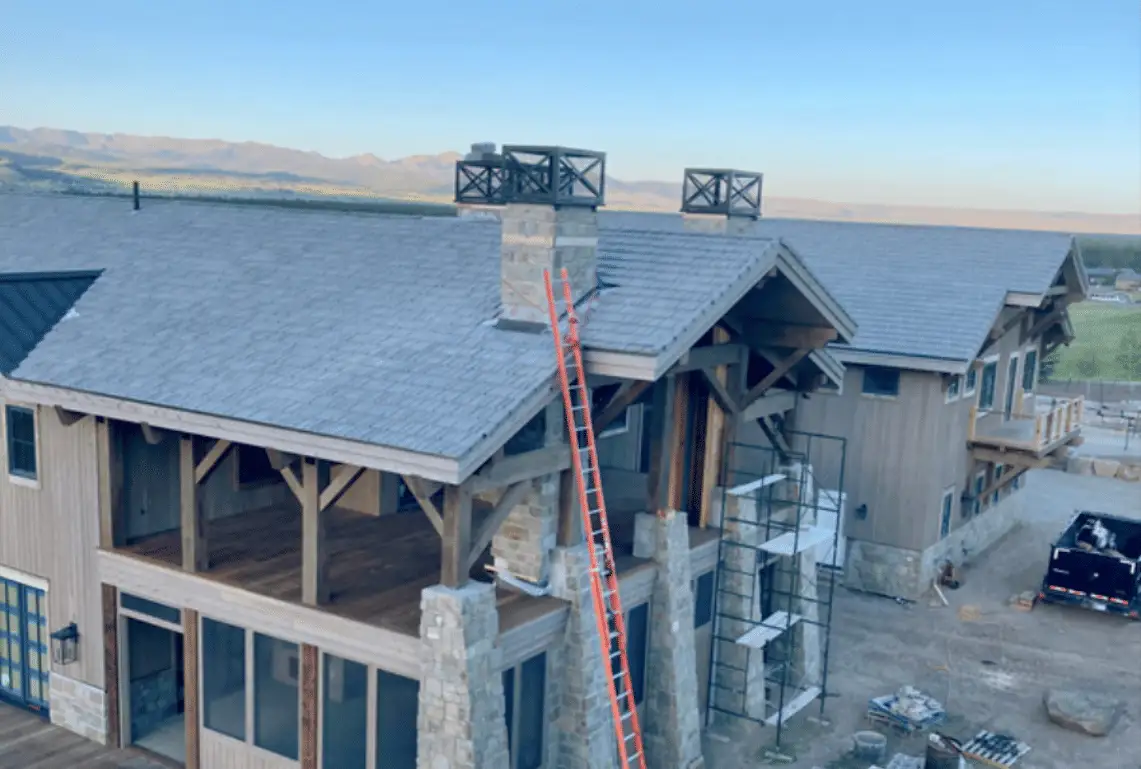Mountain home with a new grey synthetic shake roof, ladder and scaffolding