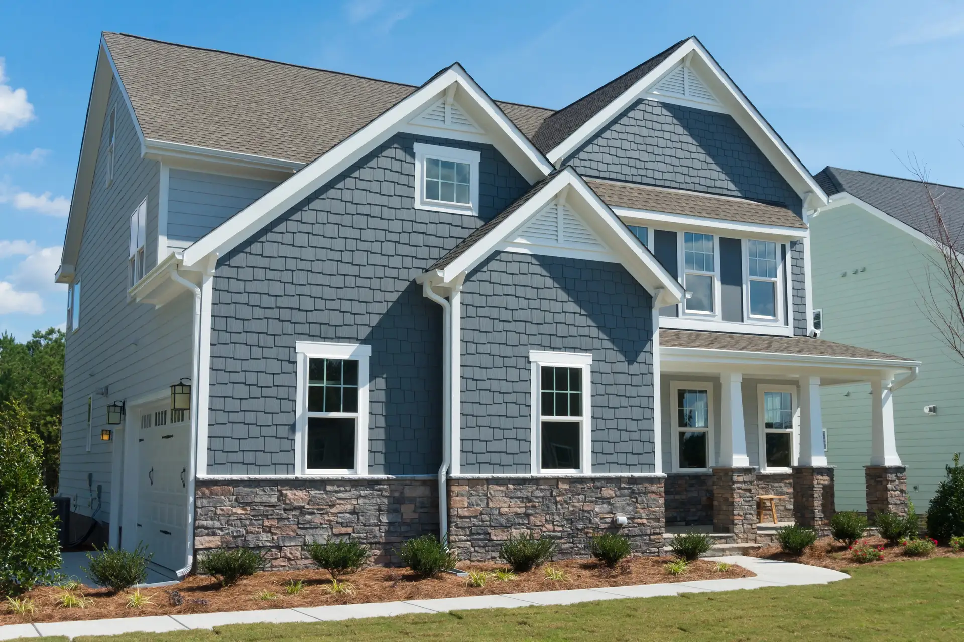 Two-storey home with blue-grey shake siding, white trim and a stone veneer base