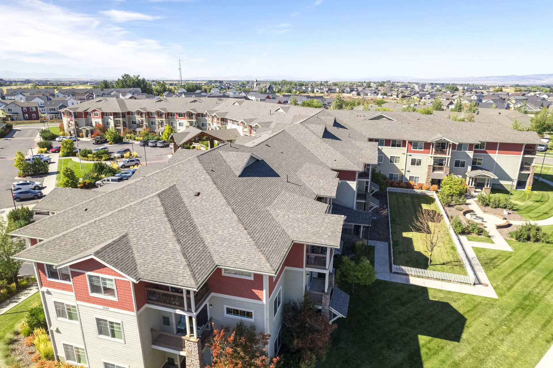 Aerial view of an apartment complex with grey shingle roofs, red and tan siding, and a courtyard lawn