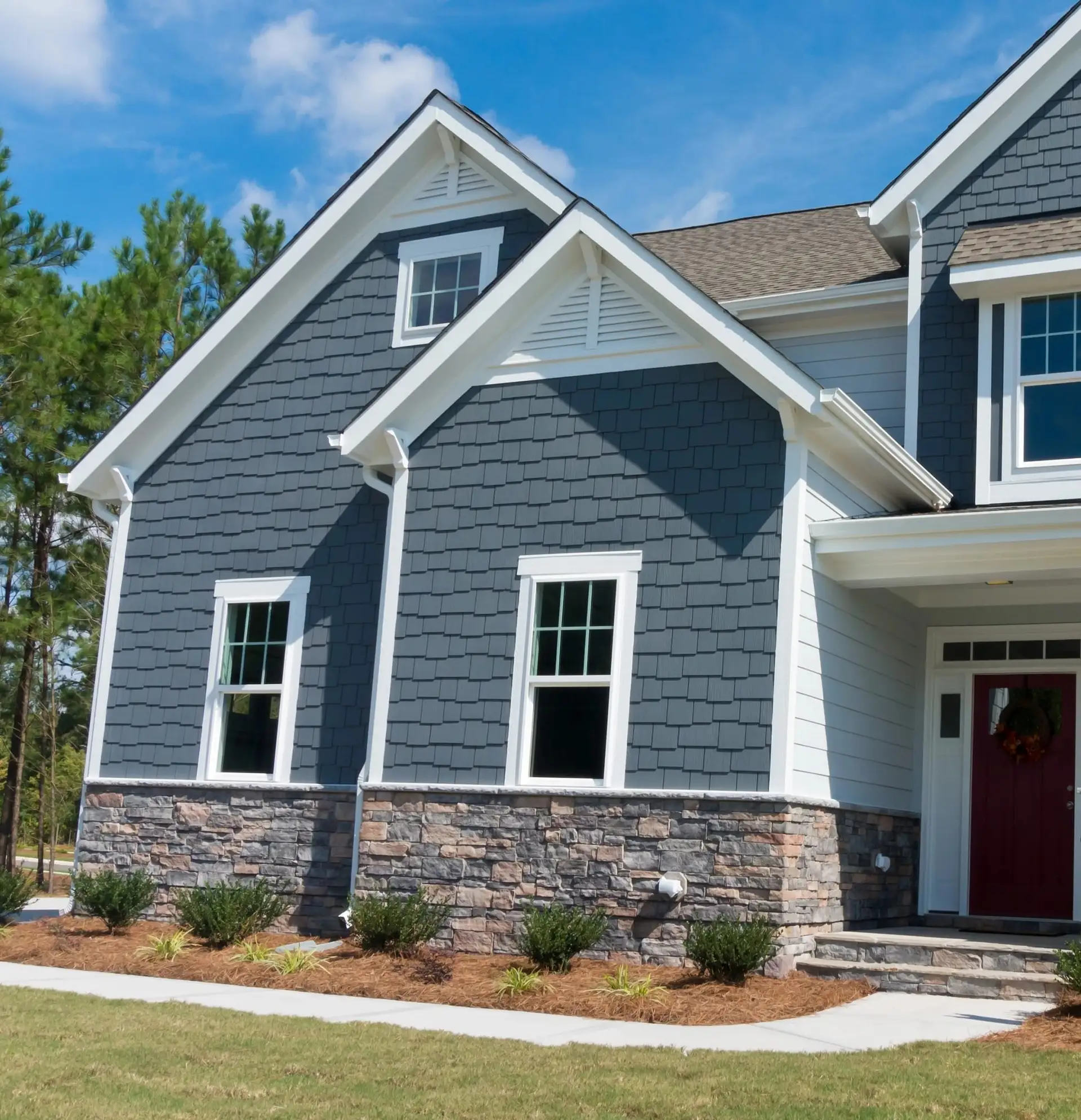 Blue-grey shake siding above a stone veneer base beside a red front door