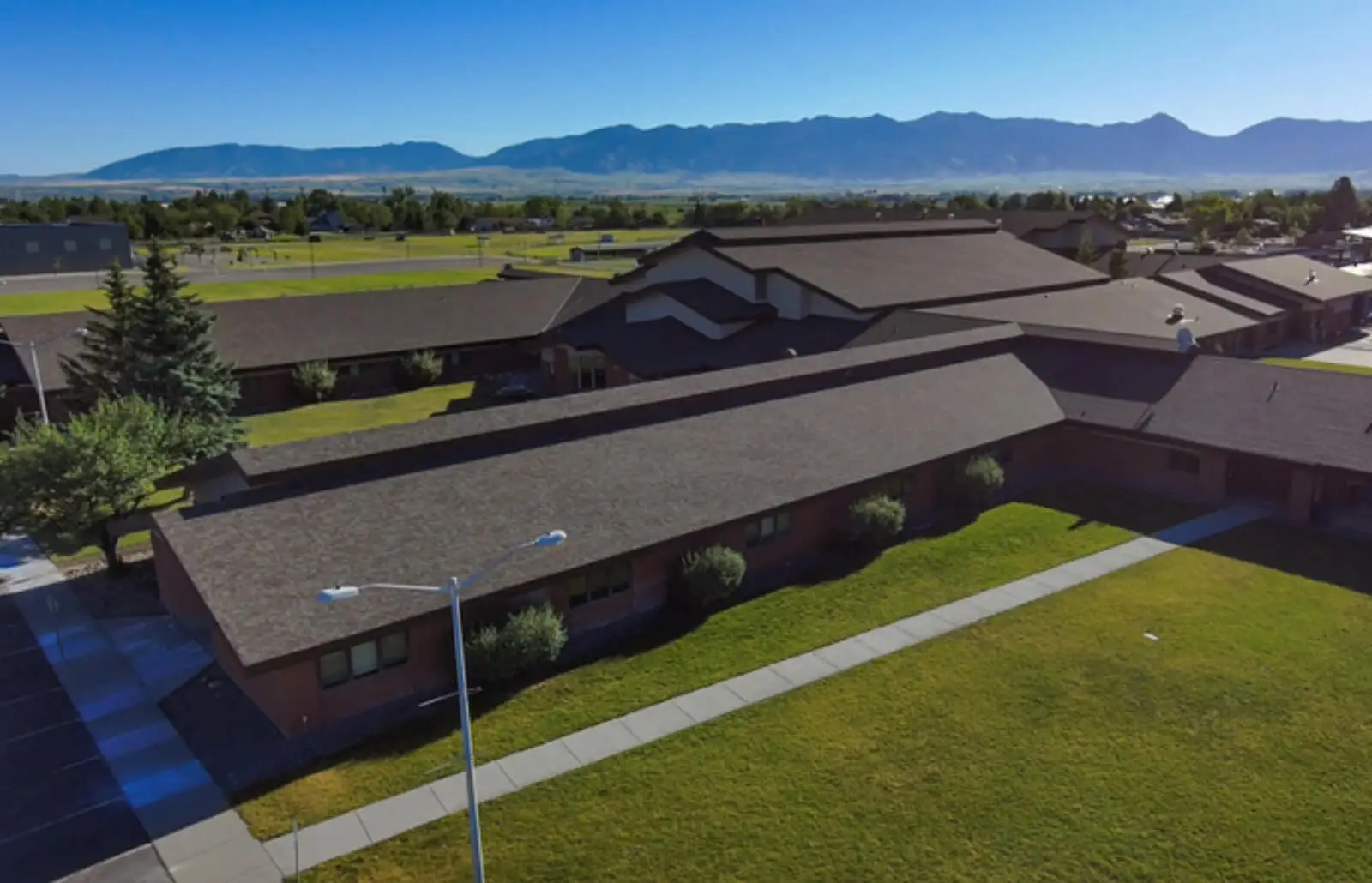 Aerial view of a long single-storey brick building with a new dark shingle roof, mountains beyond