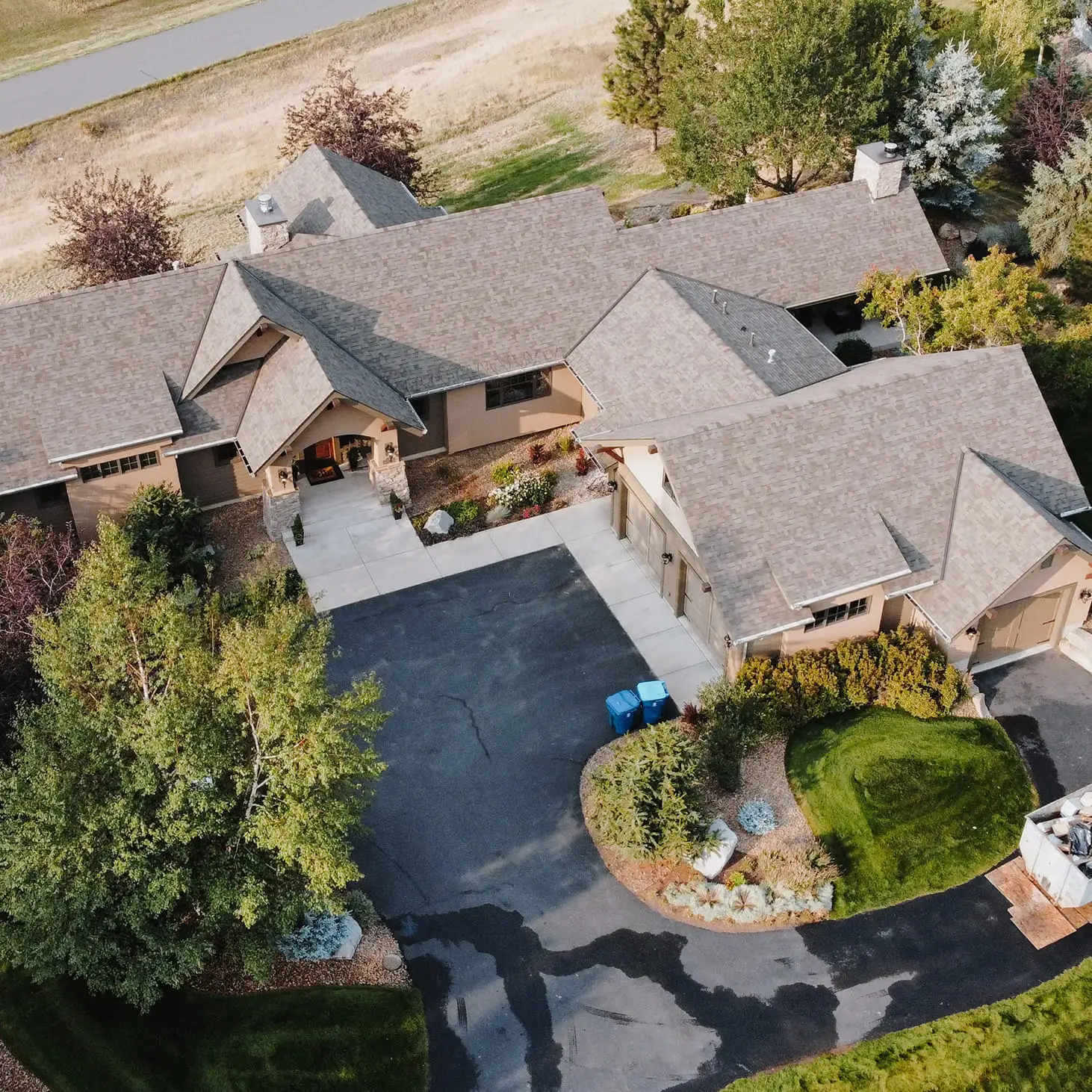 Aerial view of a large single-storey home with a new tan shingle roof and a circular driveway