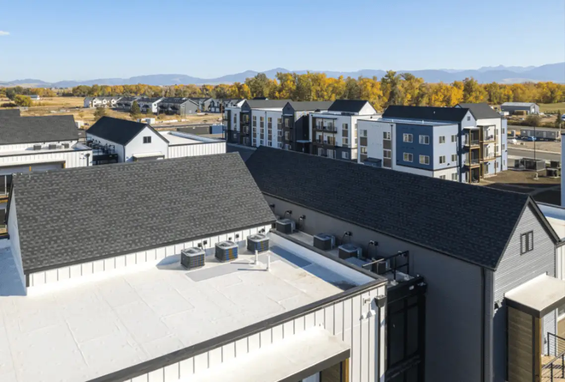 White flat roof with condenser units beside dark shingle roofs on apartments