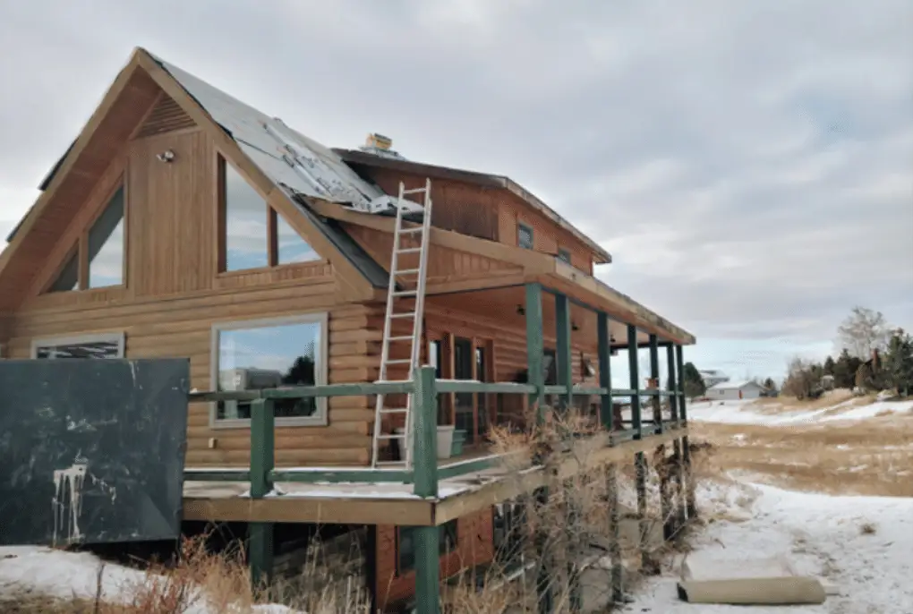 Log home roof being stripped in winter, ladder against the wall