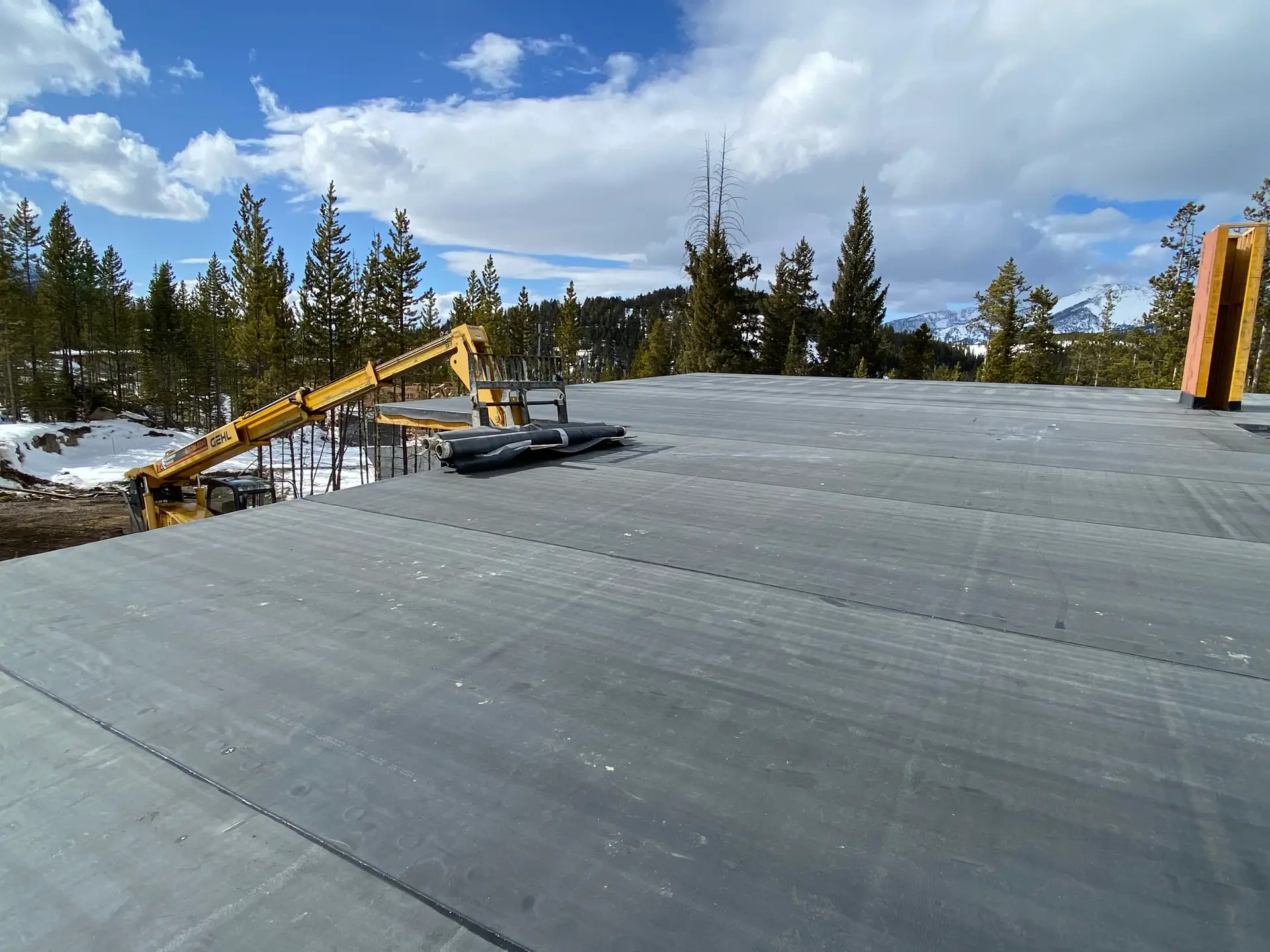 Membrane roof being installed on a flat roof, with a lift, pine trees and snowy mountains