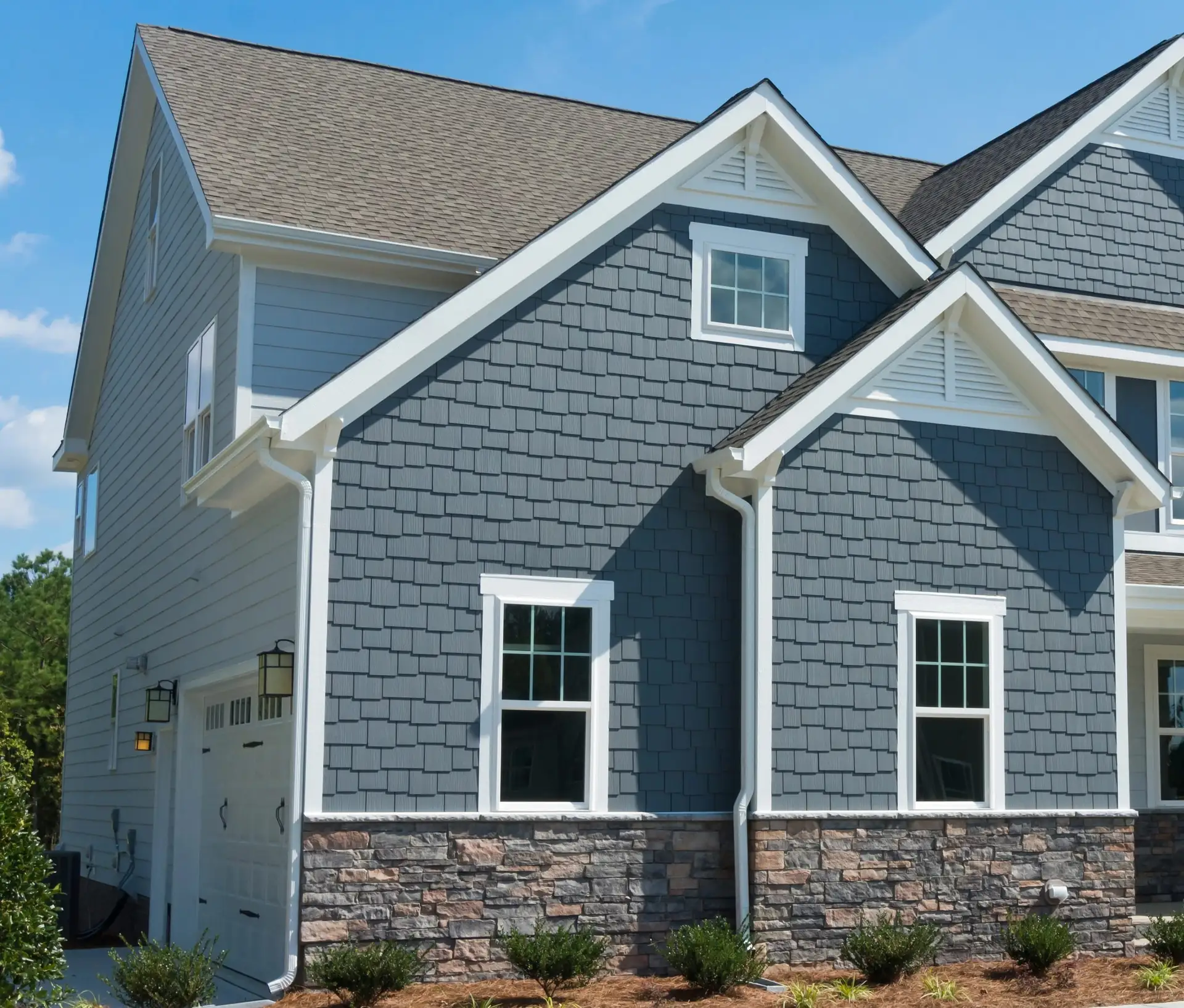 Two-storey home with blue-grey shake siding, white trim and a stone veneer base