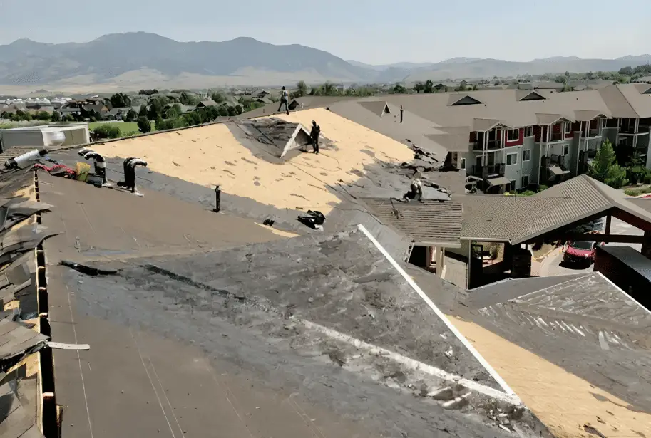 Crew tearing off an apartment roof, mountains in the distance