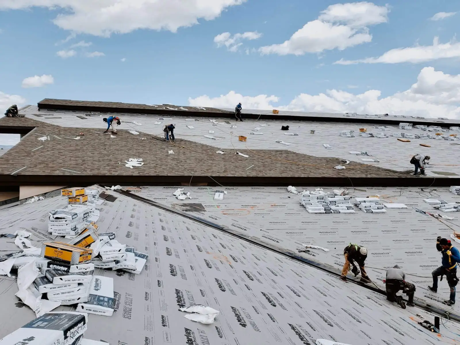 Roofing crew installing shingles over underlayment on a large roof