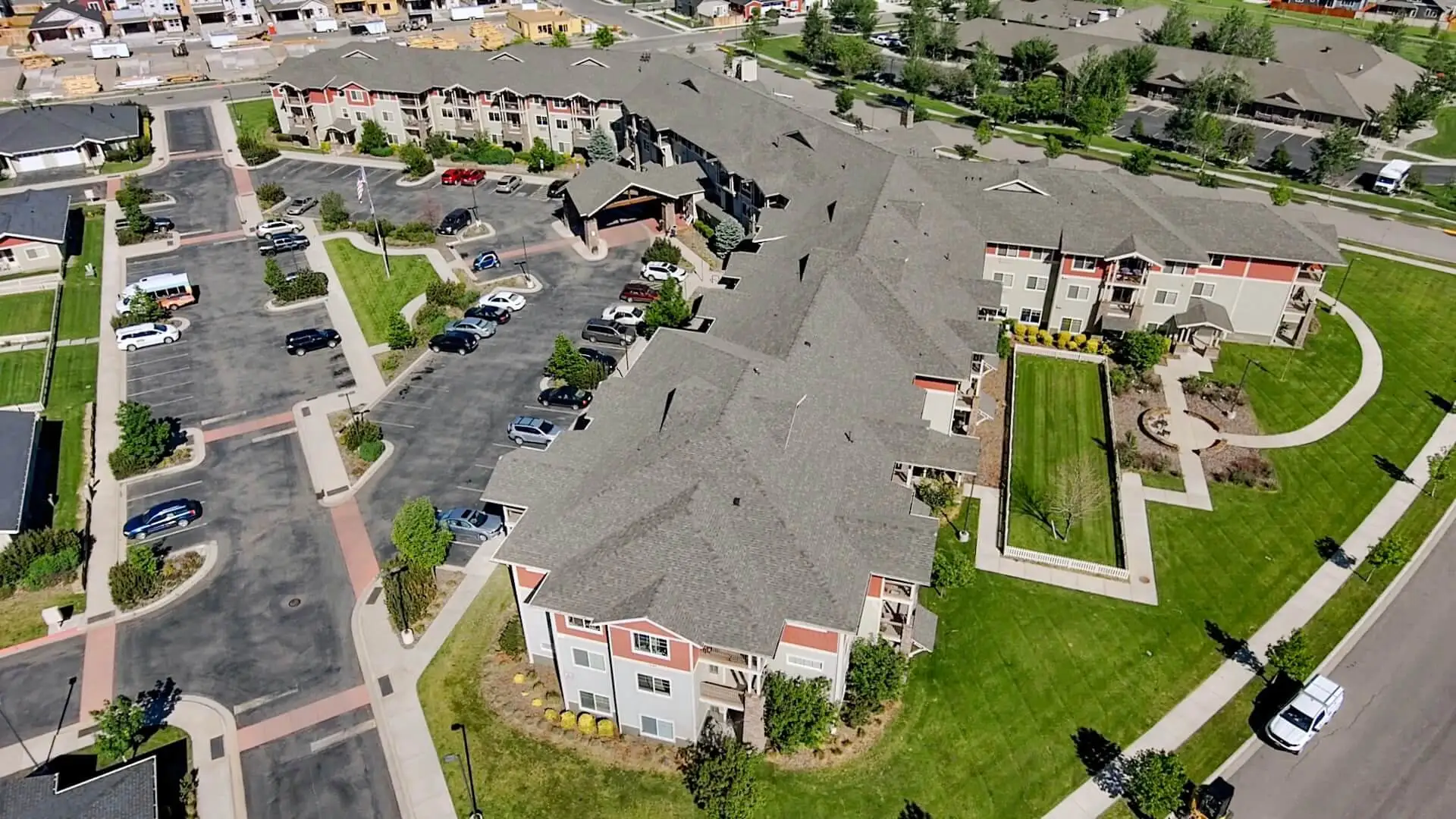 Aerial view of an apartment complex with grey shingle roofs, parking lots and a central lawn