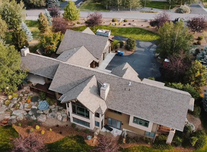 Aerial view of a large home with a light brown shingle roof and rock landscaping