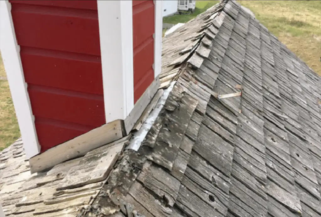 Weathered, damaged wood shingles beside a red cupola before replacement