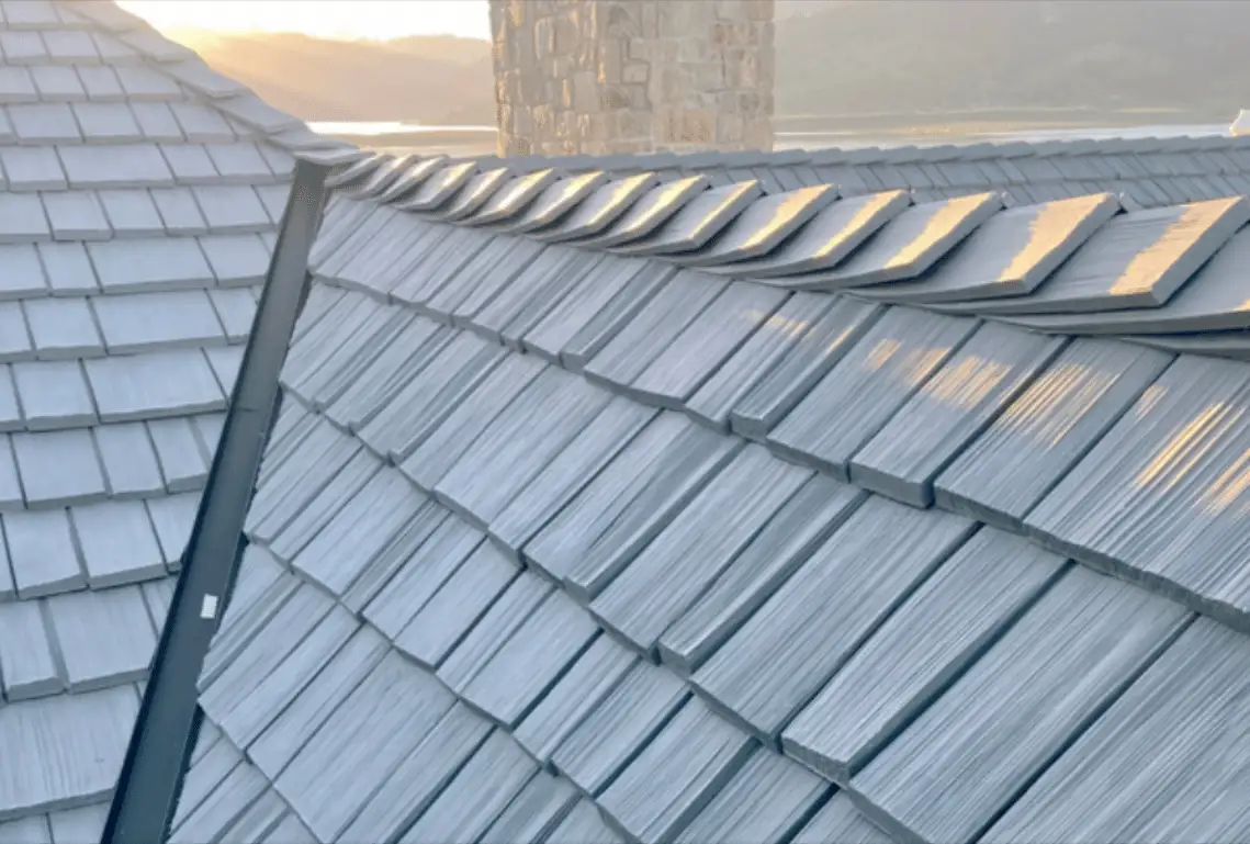Close-up of grey synthetic shakes with a metal valley and stone chimney